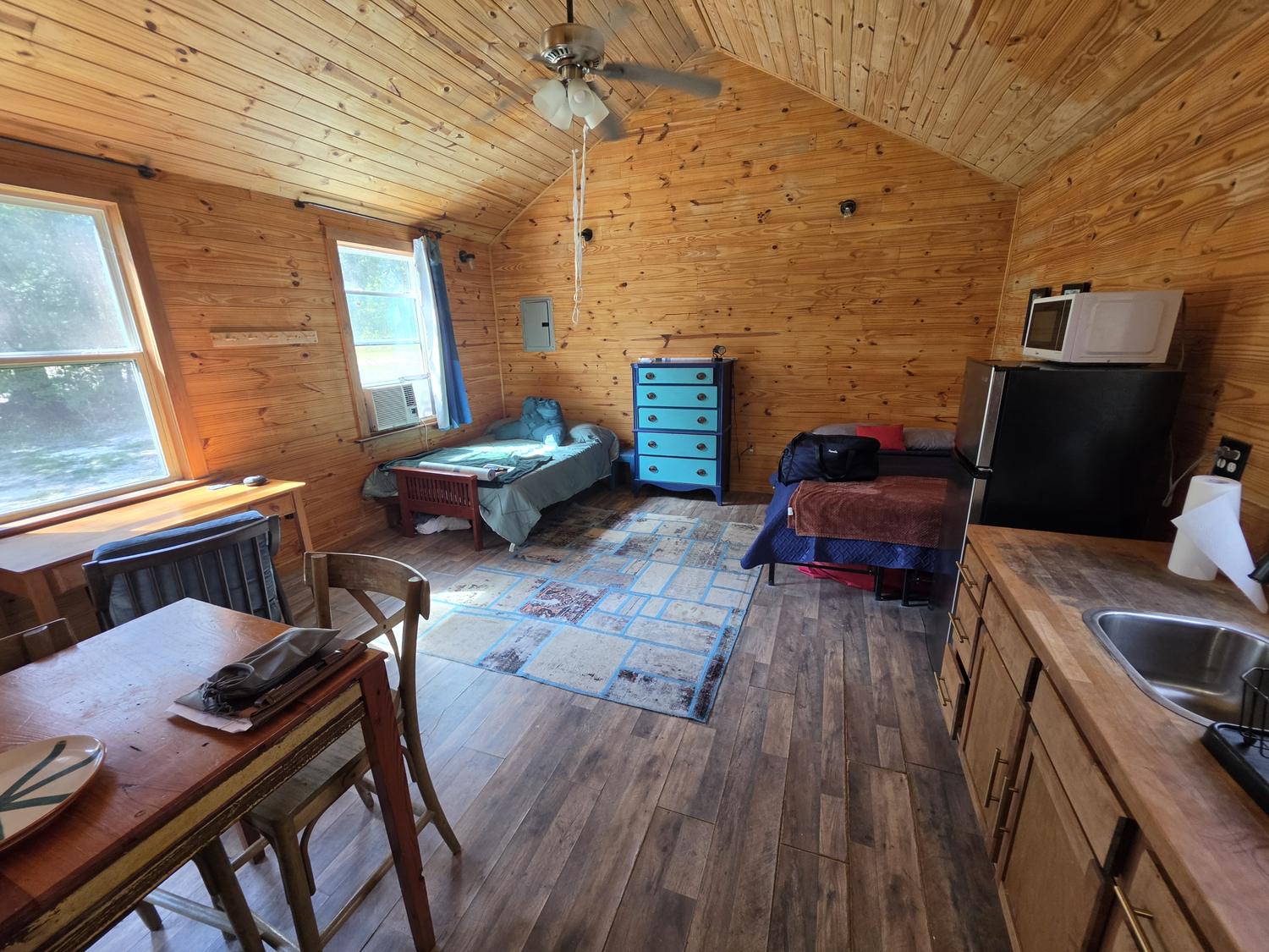 The inside of the cabin: pine walls and ceiling, two beds, a blue dresser, a small kitchen along the right wall.