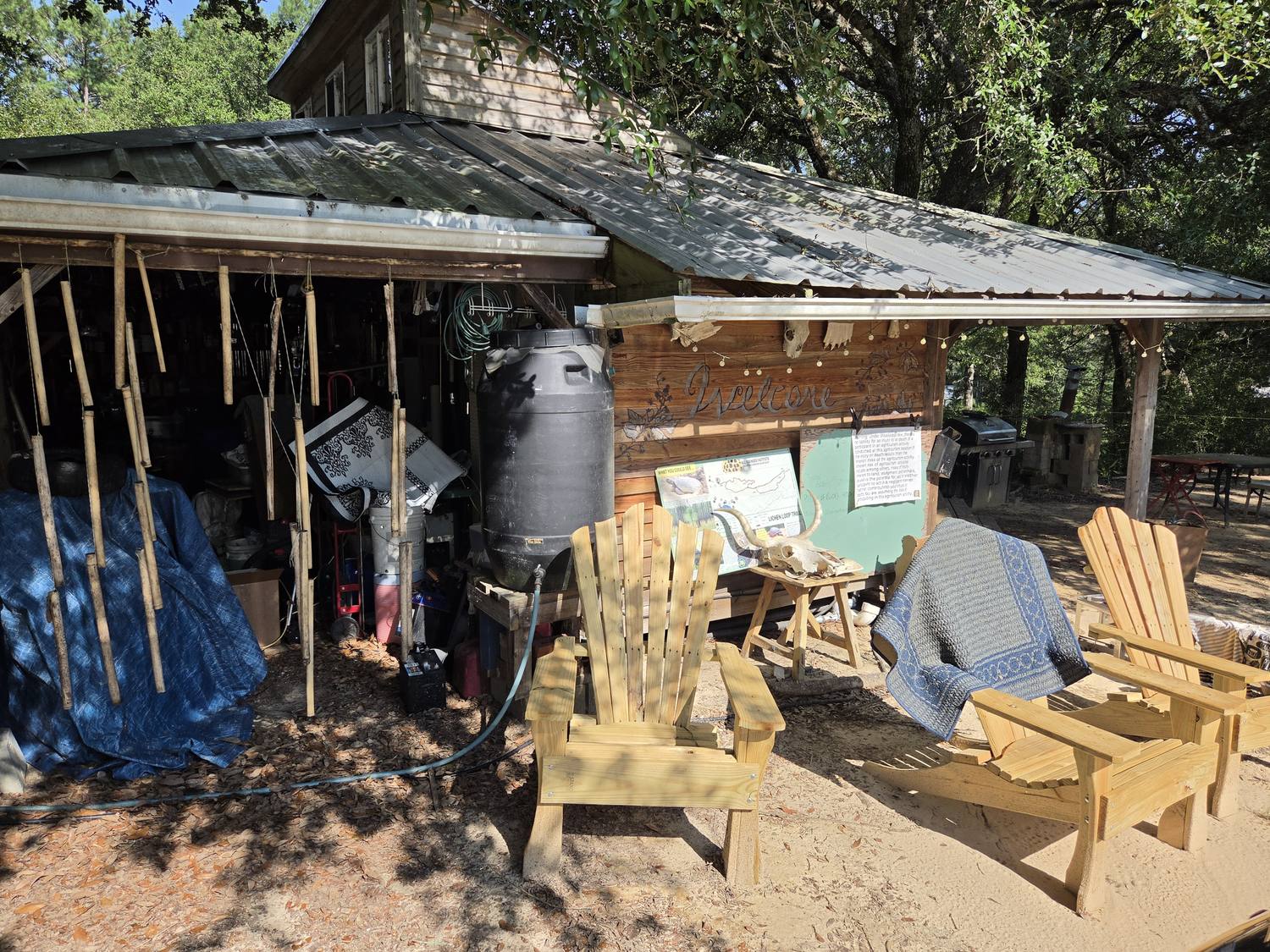 An open-sided barn hung with bamboo poles and a carved Welcome sign, with new Adirondack chairs out front on the sand.